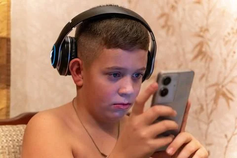 Boy using smartphone while wearing headphones at home in the evening Stock Photos