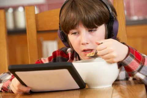 Boy Using Tablet Computer Whilst Eating Breakfast Foto stock