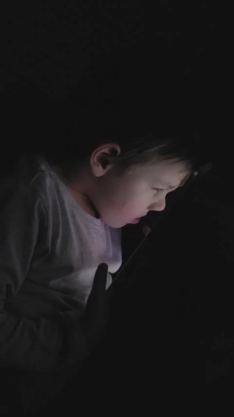 Boy using a tablet in a dark room while focused on content, showing Stock Footage 297076940