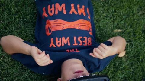 Boy using a virtual realty headset while lying outside on grass Stock Footage 275294115