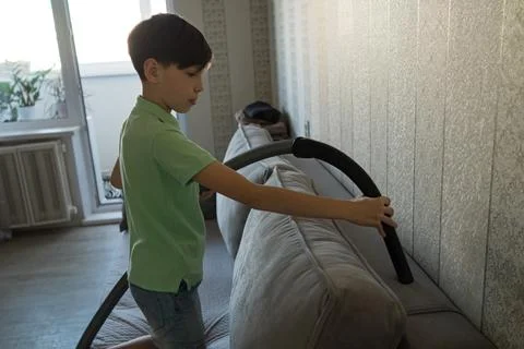Boy vacuuming sofa upholstery, learning household chores Stock Photos
