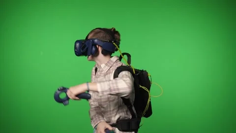 A boy in virtual reality headset is playing a video game on a green background. Stock Footage 317300501
