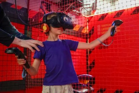 Boy in virtual reality headset plays video games in an arcade with he help of Stock Photos