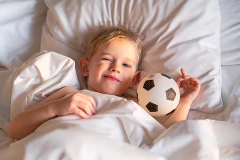 Boy wakes up and squints from the sun in an embrace with a soccer ball. Stock Photos