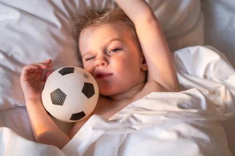 Boy wakes up and squints from the sun in an embrace with a soccer ball. Stock Photos