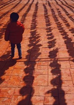 A Boy Walk Through Shadows Cast on a Vibrant Tiled Surface Foto stock