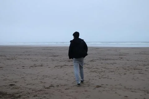 Boy walking alone on empty misty beach Foto stock