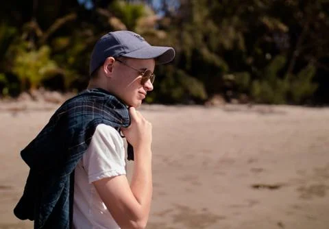 Boy walking along the beach with sunglasses and a hat Stock Photos