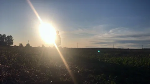A boy walking along the meadow alone, backlit at sunset. Sun shining from behind Stock Footage 116709532