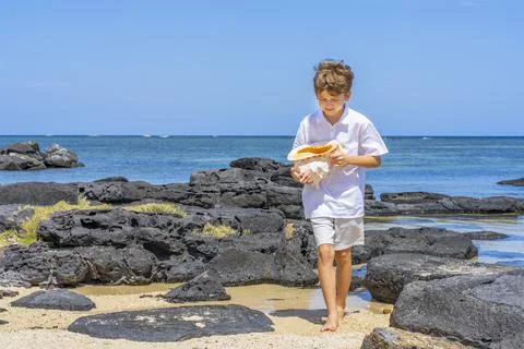 A boy walking with a big seashell in his hand on the tropical beach. Stock Photos
