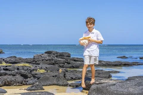 A boy walking with a big seashell in his hand on the tropical beach. Stock Photos