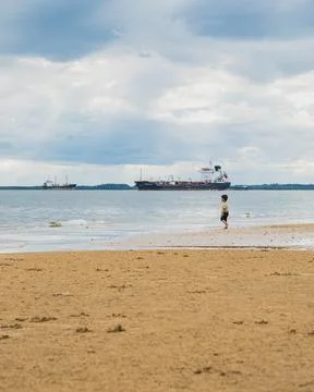 A boy walking down the beach in a cloudy day. Stock Photos