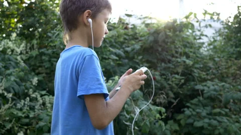 Boy walking down the street uses the phone and listening to music Stock Footage