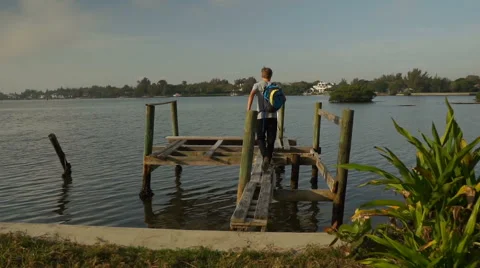 Boy walking on an old dock toward water Video stock 64107407