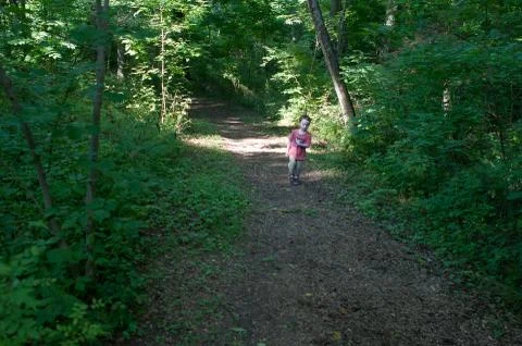 Boy walking on pathway in green open space with mature trees on a sunny day with Stock Photos
