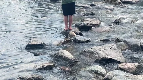 Boy walks across rocks on a river or stream Vidéo 236729012