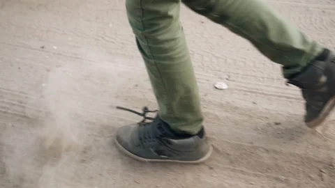 A boy walks along a sandy road kicking up dust with his feet Vídeo Stock 128016307