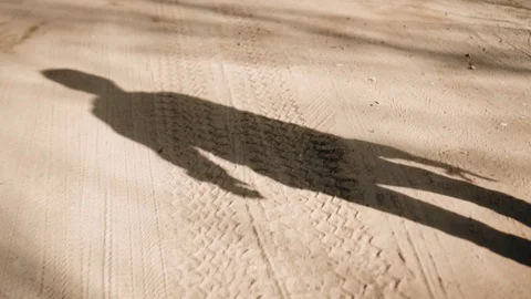 A boy walks along a sandy road. Close - up of his shadow. Very cool. Stock Footage 128016308
