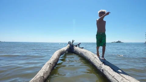 The boy walks balancing on the logs floating in the water in lake. Stock Footage 137575053