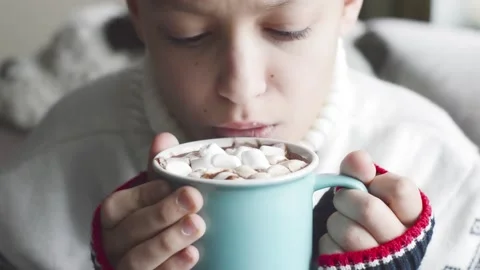 A boy in a warm sweater drinks hot cocoa with marshmallows. Stock Footage 144807094