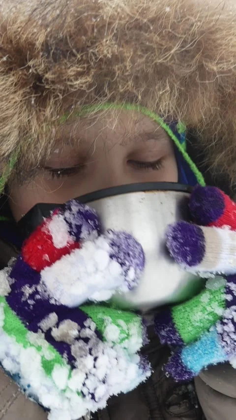 Boy in a warm winter jacket on the hood drinks hot tea from a thermos winter Stock Footage 317849923