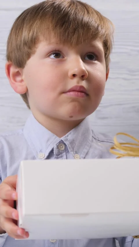 The boy was given a box with a gift he looks at it on a wooden background. Video stock 157625688