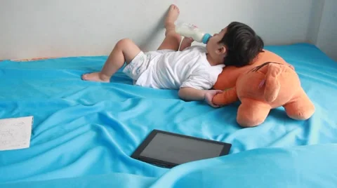 The boy was lying on the bed and drinking milk from a bottle. Stockbeeldmateriaal 55425062