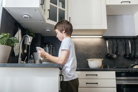 Boy washing dishes in kitchen, learning domestic responsibility Stock Photos