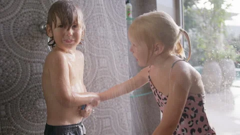 Boy washing under a shower stream while a girl dances and waves her hands nearby Stock Footage 296716887