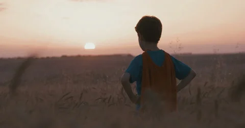 Boy watches the setting sun dressed as a superhero Stock Footage 63272976