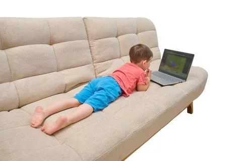 Boy watching cartoon on laptop while lying on beige sofa. Child using compute Stock Photos
