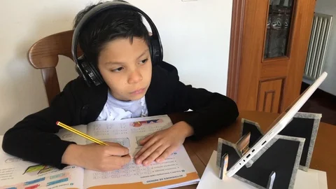 Boy watching a tutorial on his tablet with headphones to do his homework 動画素材 126627184