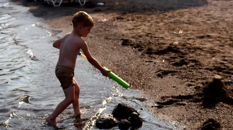 Boy with a water gun pours sand castle Stock Footage 30556592