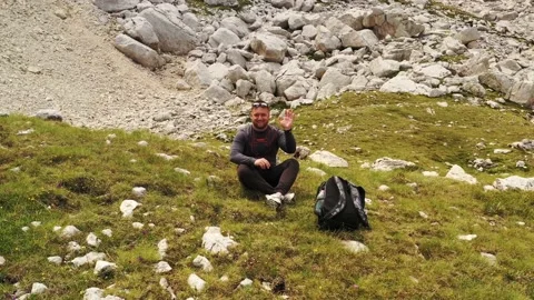 Boy waving to the drone as it moves away on a mountain slope Video stock 136921749