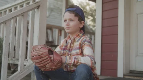 Boy Wearing a Baseball Cap and Glove While Sitting on a Porch Stock Footage 208769409