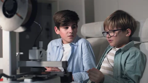 A boy wearing glasses explains to his friend how a 3D printer works Stock Footage 335374609