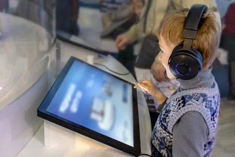 Boy wearing headphones interacts with interactive screen at an exhibit Stock Photos
