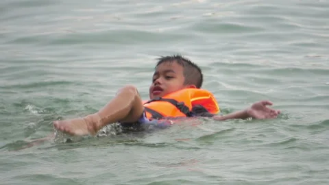 Boy wearing life jacket playing in water at swimming sea Stock Footage 251552983