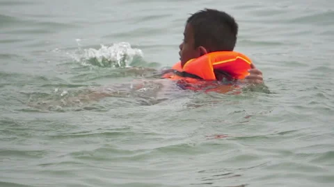 Boy wearing life jacket playing in water at swimming sea Stock Footage 251553070