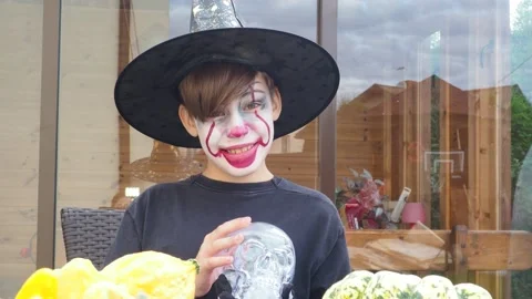 Boy wearing scary jocker or clown makeup and halloween costume play with scull Video stock 141436290