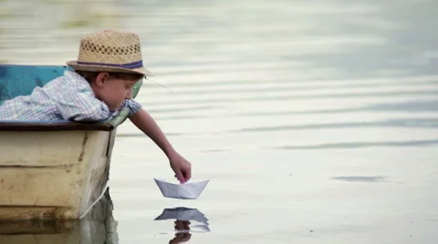 Boy wearing wicker hat sitting in the boat setting his paper boat on a journey Stock Footage 60605030