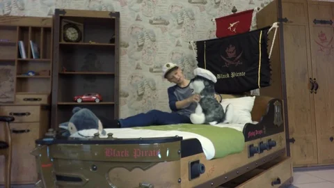 The boy wears a captain's cap. Bed in the form of a pirate ship. 库存影片 84264798