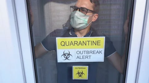 Boy wears disposable face mask, stay at home, look out at street through glass Stock Footage 131476691