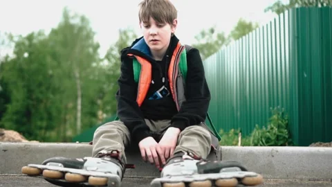 The boy went on roller skates and rests sitting by the road. Sports lifestyle. Stock Footage 131281100