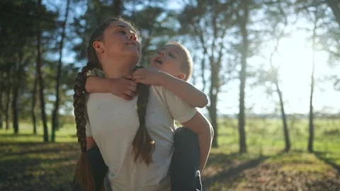 Boy whispers to sister outdoors. Happy girl smiles hearing brother. Child laugh Stock Footage 346947053