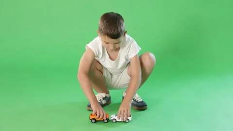 Boy in white clothes playing with toy cars on green background Stock Footage 346120513