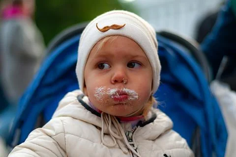 A boy in a white hat smeared all his cheeks in white cream from a cake Foto stock