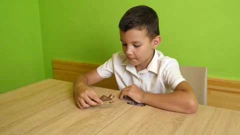 Boy in a white shirt eats a chocolate bar while sitting at a table and enjoyi Stock Footage 338104519