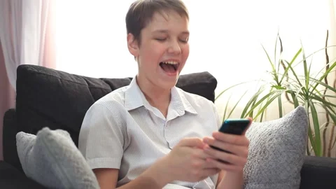 Boy in a White Shirt Laughs While Watching A Video on a Smartphone Screen. Stock Footage 153325446
