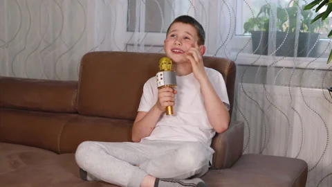 Boy in white shirt singing using microphone at home Stock Footage 153581063
